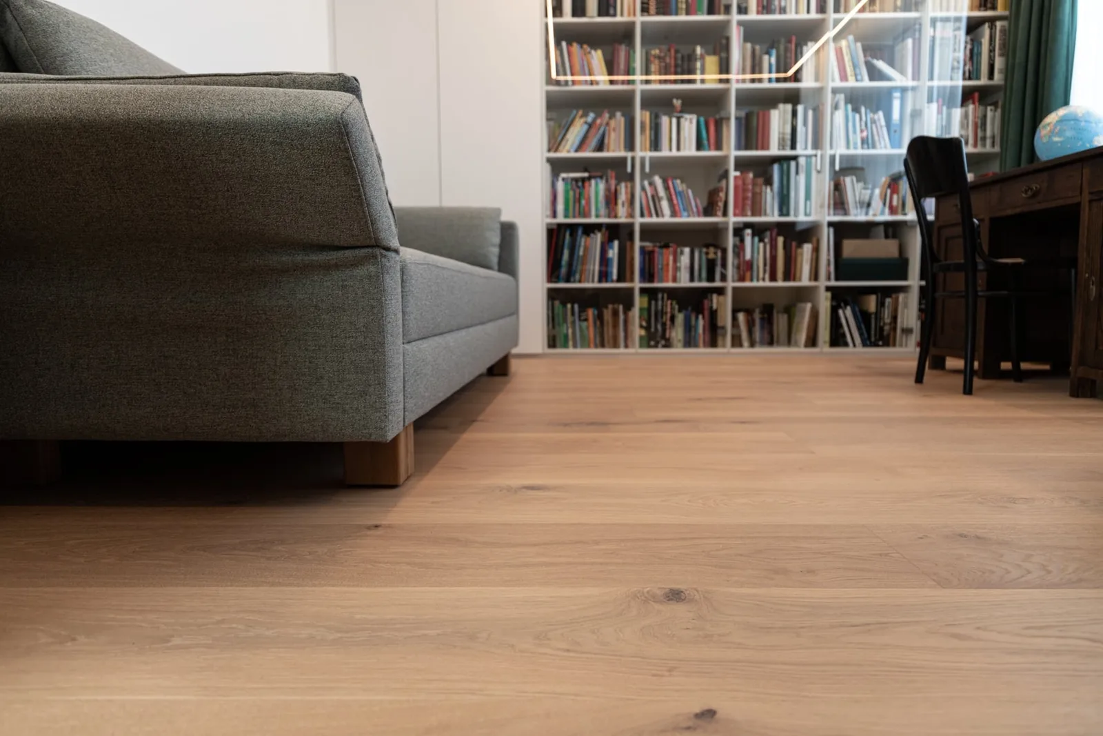 Wohnraum mit hellem Holzboden, Sofa und Bücherregal