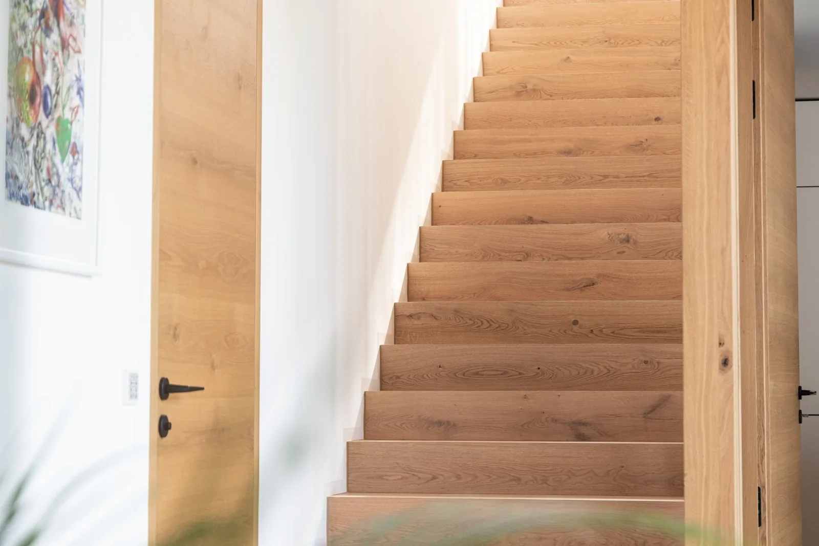 Holzstiege mit hellen Stufen neben einer weißen Wand
