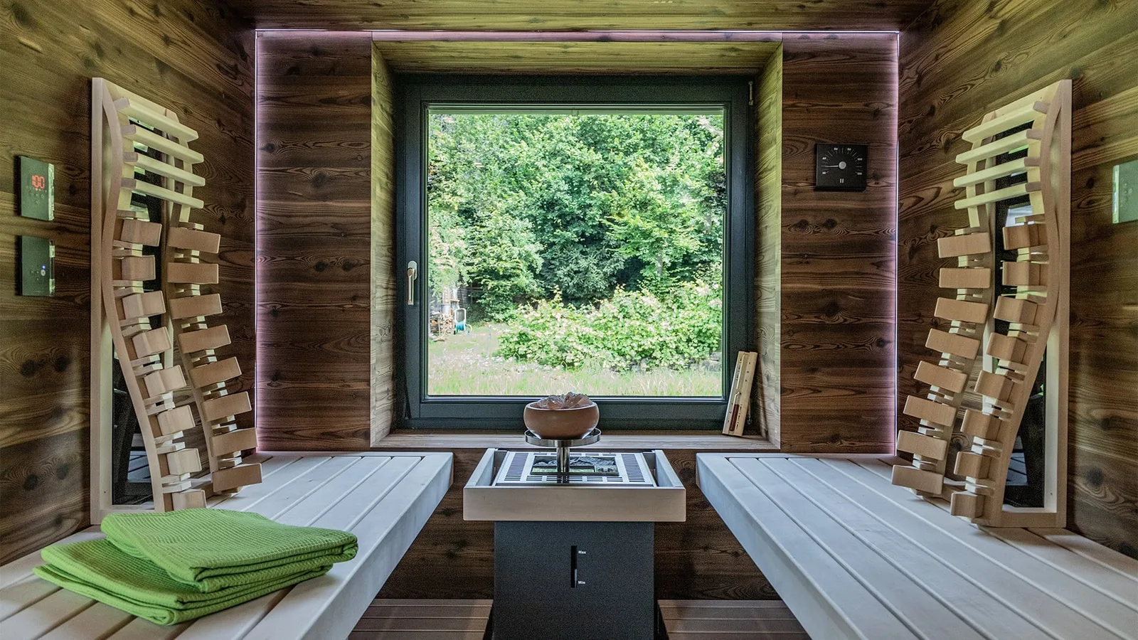 Sauna mit dunklen Holzwänden, hellen Liegen und großem Fenster ins Grüne