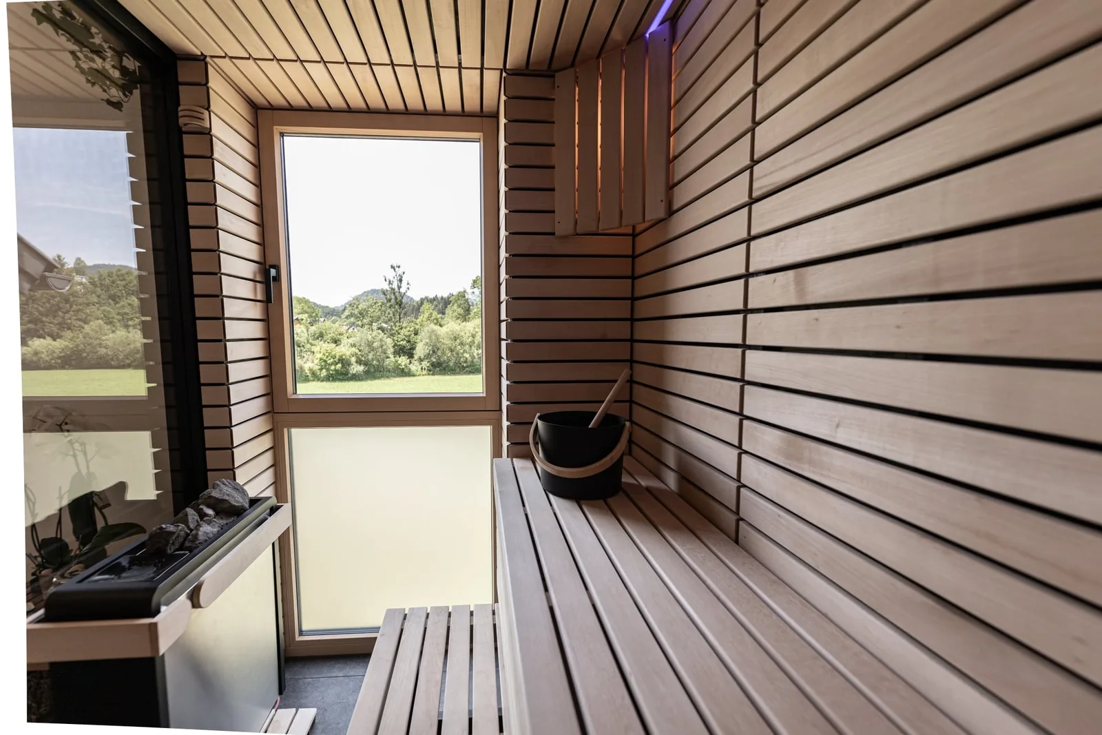 Sauna mit waagrechten Holzlatten, Fenster und Aufgusskübel