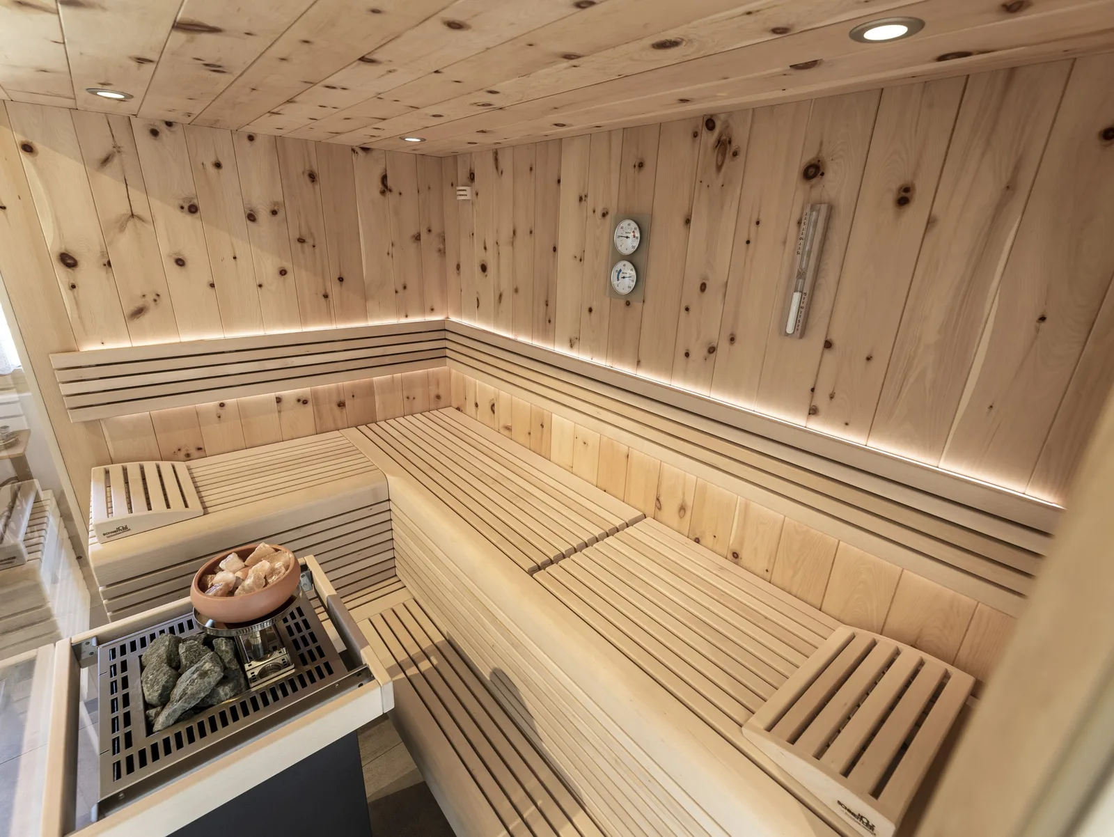Sauna aus hellem, astigem Holz mit Liegen und Ofen