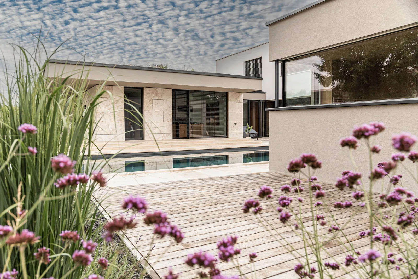 Holzterrasse mit Gräsern und Blumen vor einem Haus